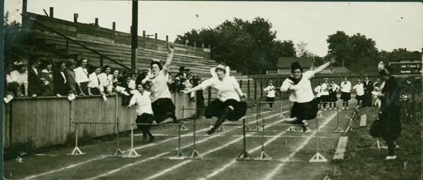 black and white photograph of three women in mid-air during a hurdling race; fourth competator follows