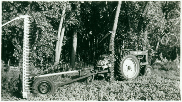 A photograph of a double sickle bar mower built to be with an extra arm in order to minimize the number of passes needed to mow a field.