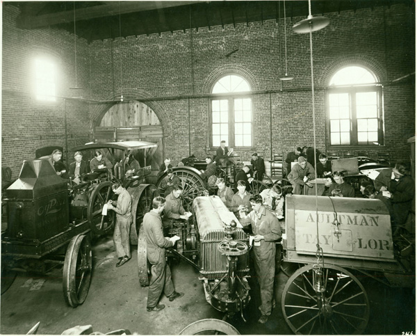 A photograph of men working in a machine shop on some very early steel wheeled tractors.