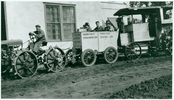 A photograph of an earlier test car and dynamometer. In the background is the
               original Tractor Test Lab building, now home of the Lester F. Larsen Tractor Test and
               Power museum.